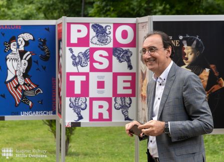 fotografia. art piknik w willi decjusza. plenerowa wystawa plakatów teatralnych. mężczyzna w garniturze stoi przed ustawionymi w rzędzie plakatami.